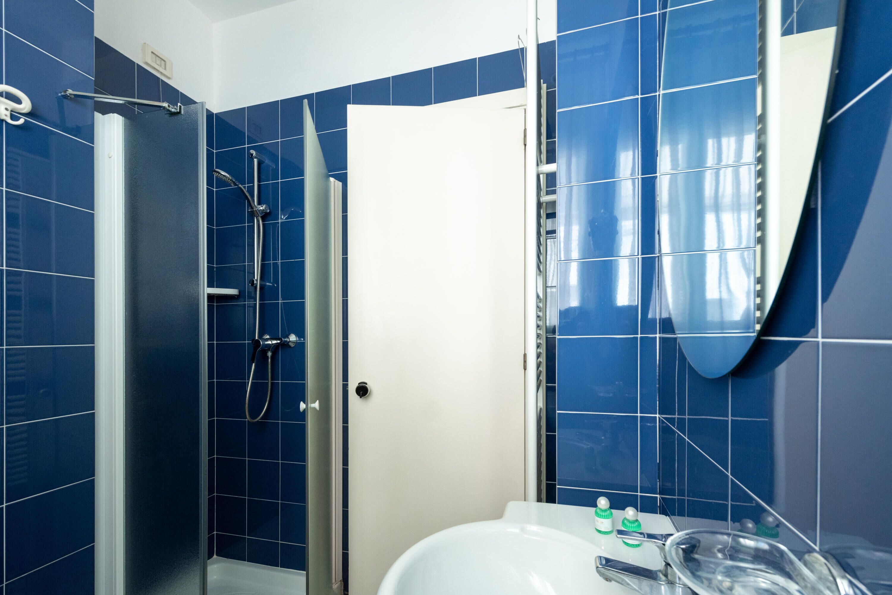 Une salle de bain avec des carreaux bleus, un lavabo blanc et une cabine de douche en verre.
