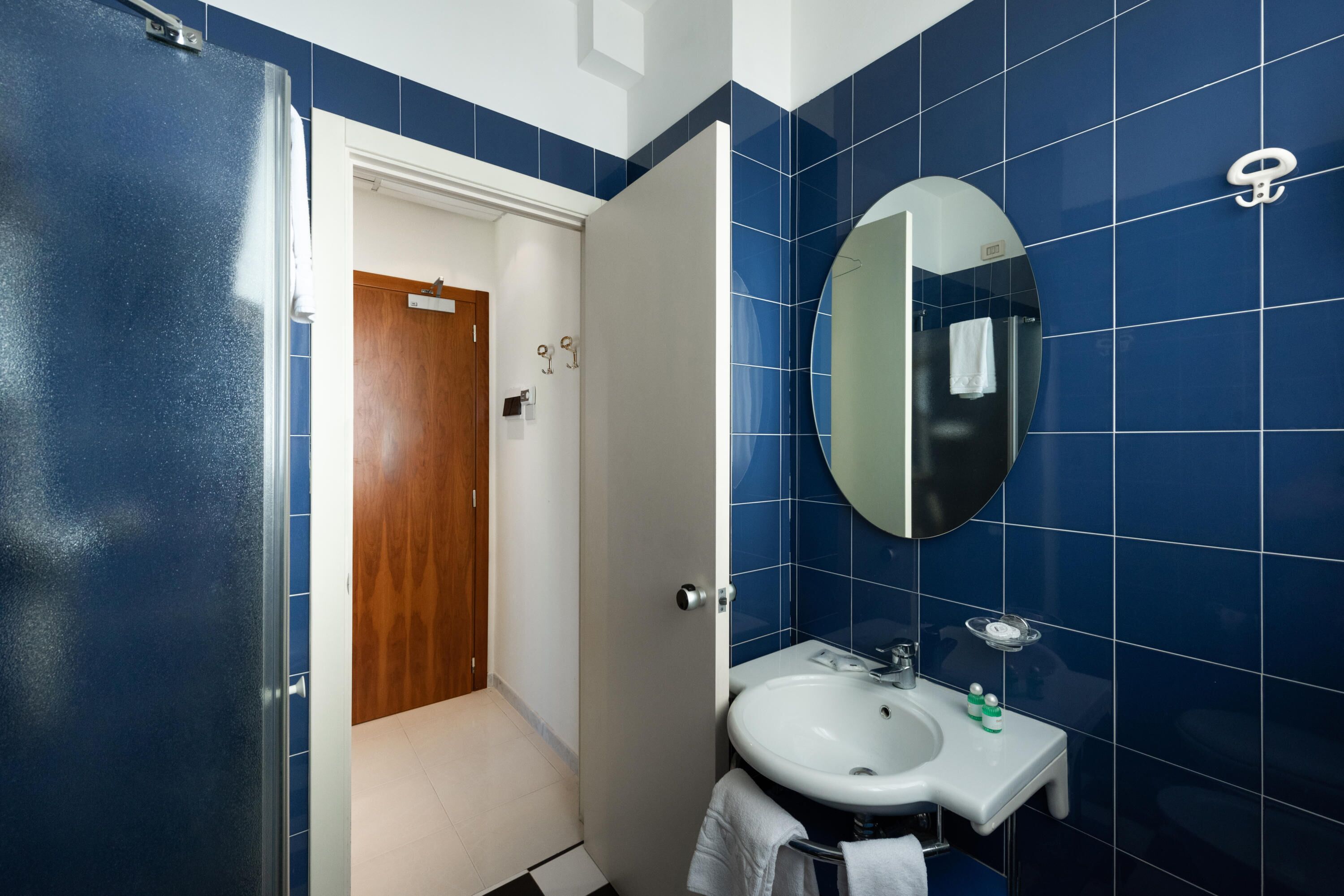 Un baño con azulejos azules, un lavamanos blanco, un espejo y un perchero para toallas.