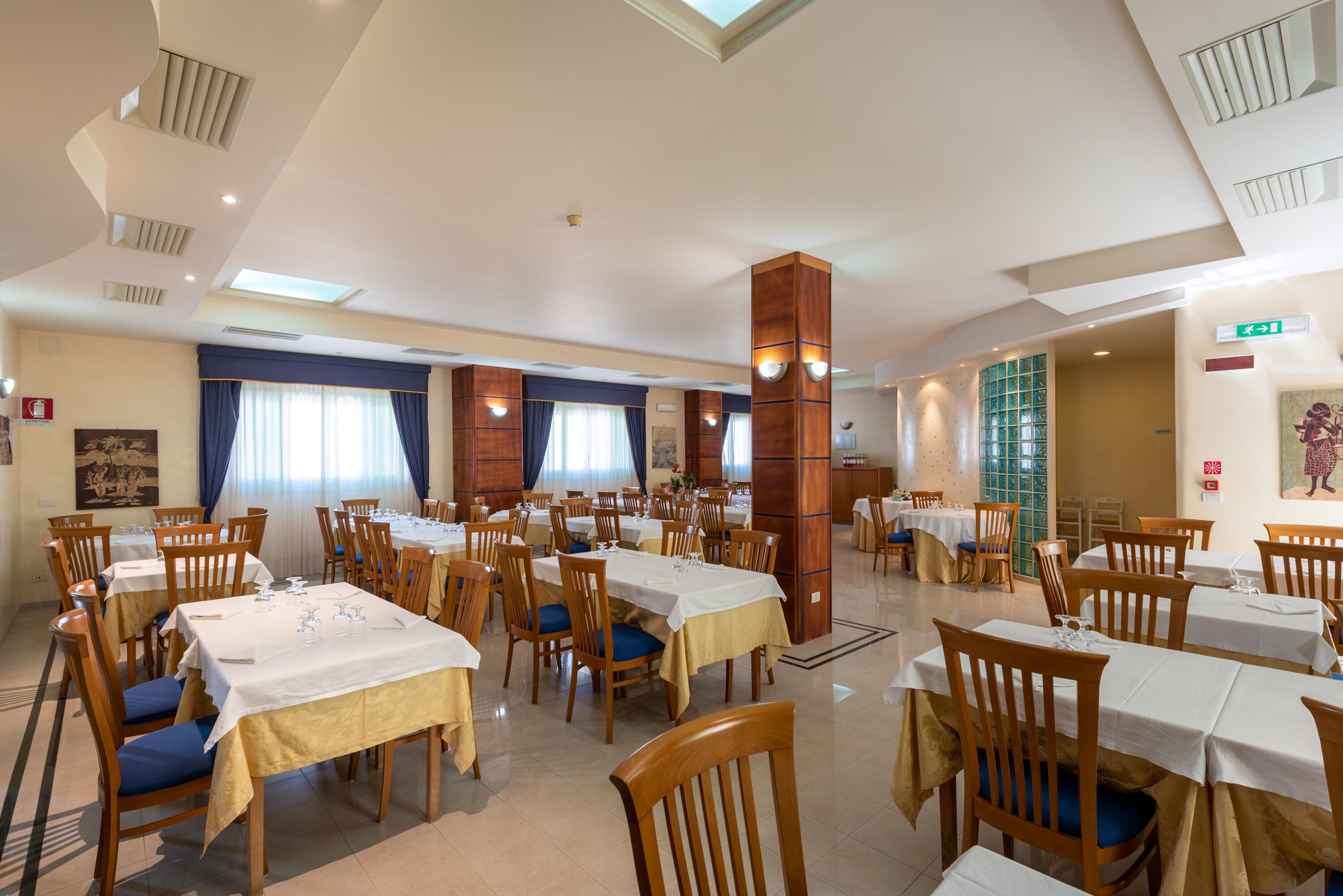 A spacious dining area with multiple tables and chairs, a high ceiling with skylights, and a large wooden pillar.