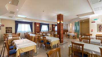 Un vaste espace dédié à la salle à manger, avec de nombreuses tables et chaises, un haut plafond agrémenté de lucarnes et une grande colonne en bois.