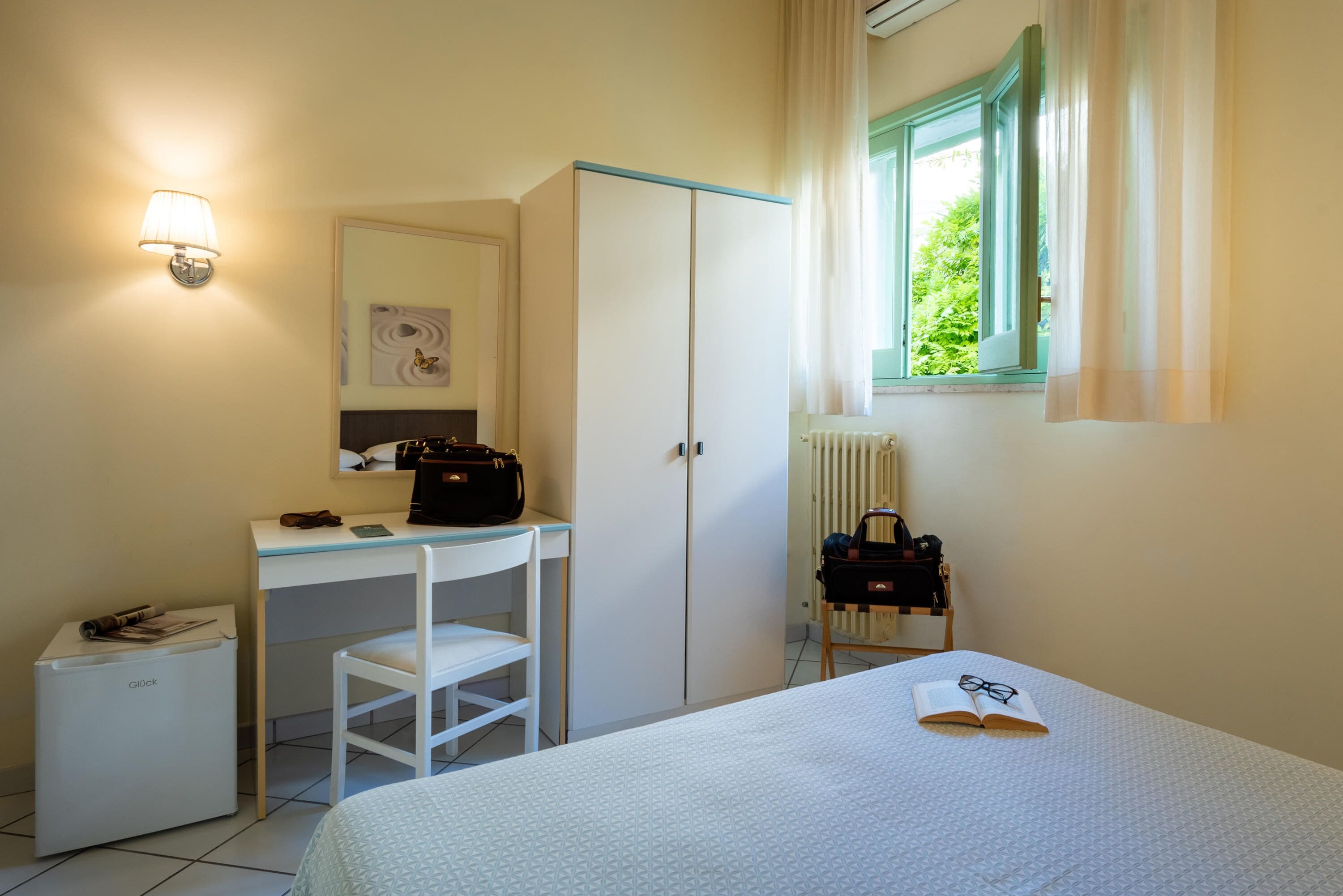 Une chambre à coucher comprenant un lit, un bureau, une armoire, un radiateur et une fenêtre avec des rideaux.