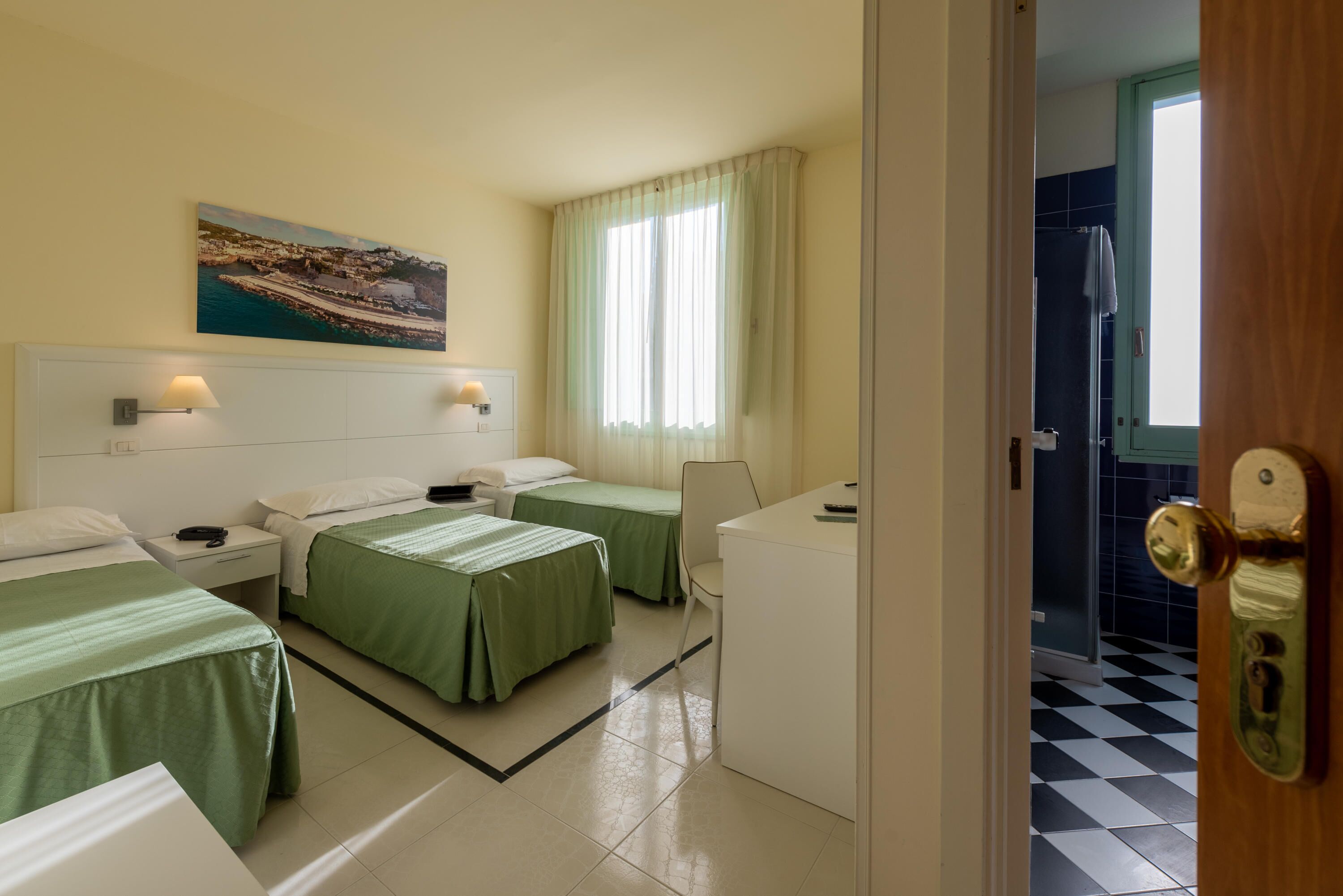 Een hotelkamer met twee eenpersoonsbedden, een bureau, een stoel, een nachtkastje, een lamp en een raam met gordijnen.