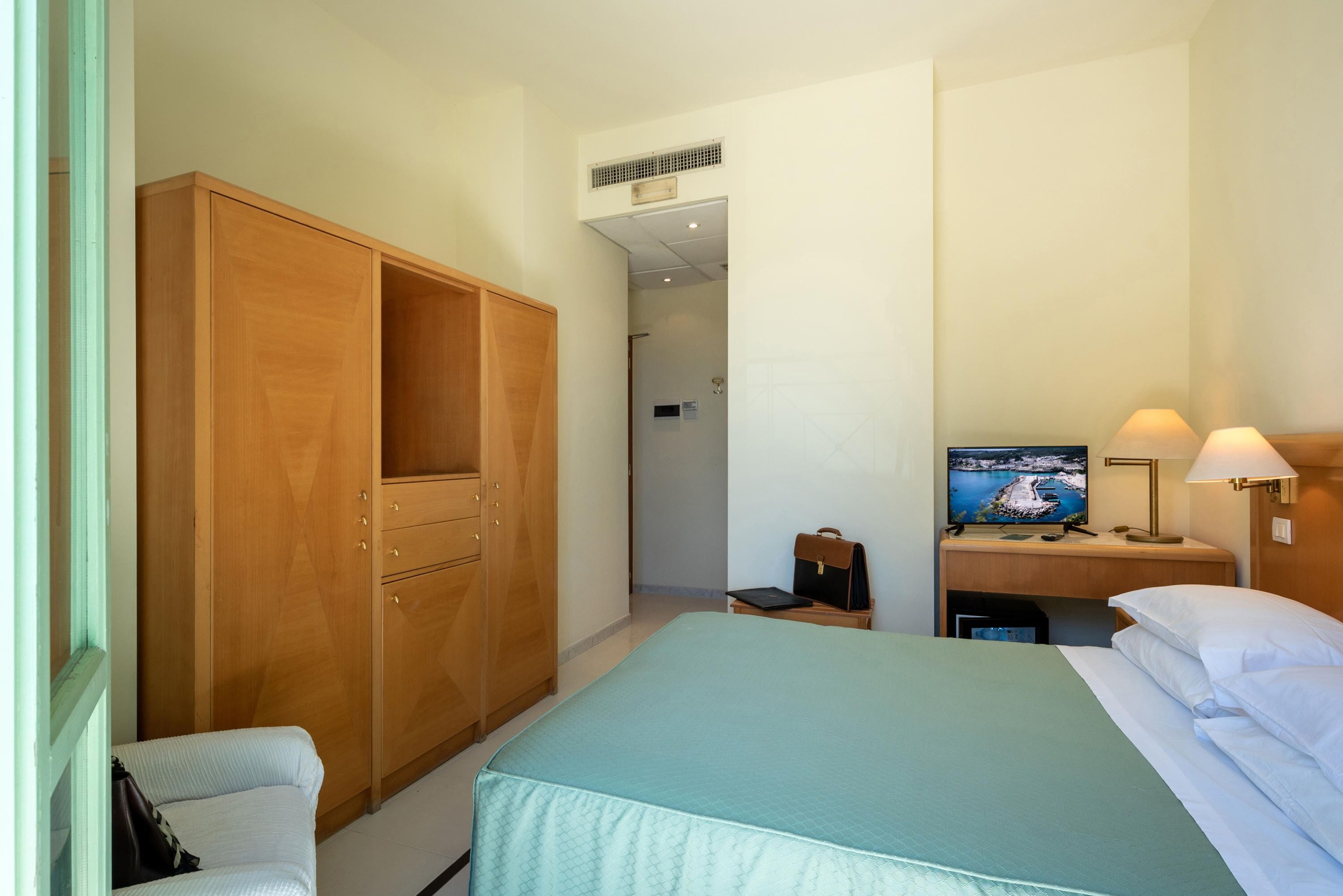 Habitación de hotel con cama, armario, escritorio con televisor y lámpara.