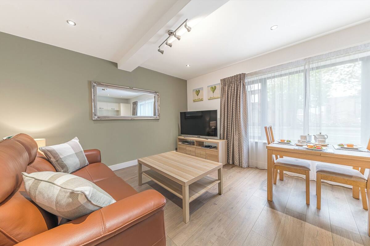 A modern living room with a sofa, coffee table, TV, and dining area with a table and chairs.