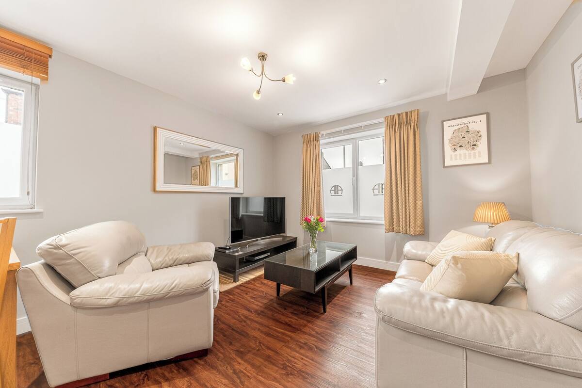 A modern living room with two leather sofas, a glass coffee table, a flat-screen TV, and a wooden floor.