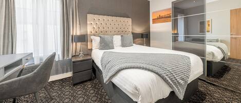 Moderni hotellihuone, jossa on suuri sänky, työpöytä ja tuoli.