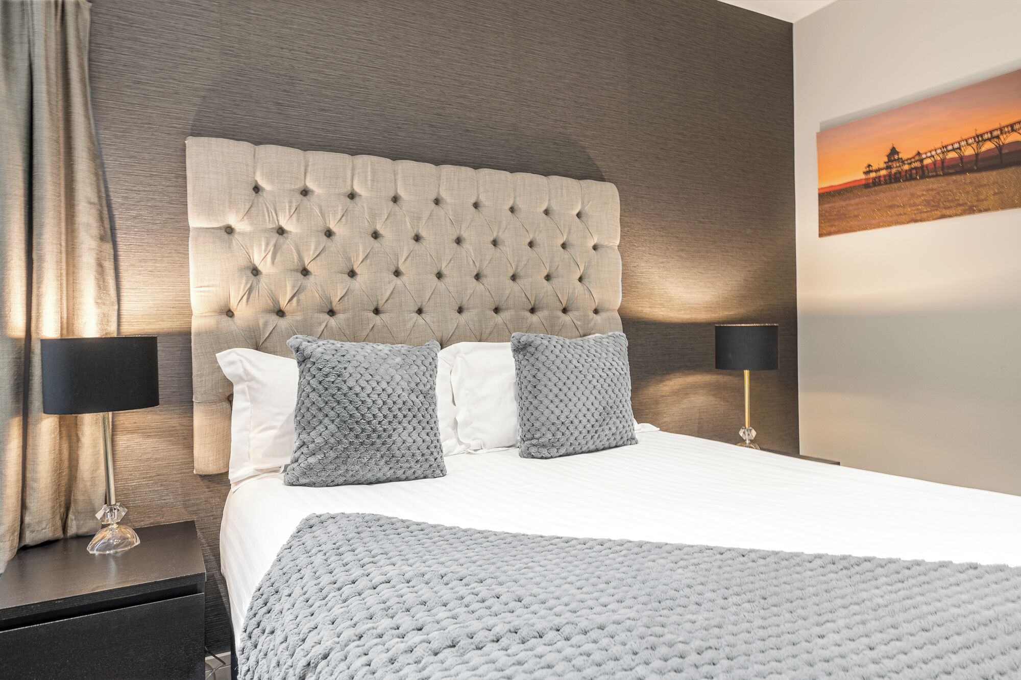A neatly made bed with a tufted headboard, two pillows, and a blanket. There are two bedside tables with lamps.