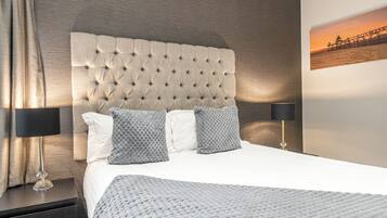 A neatly made bed with a tufted headboard, two pillows, and a blanket. There are two bedside tables with lamps.
