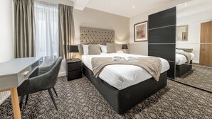 Habitació d'hotel moderna amb un llit gran, un escriptori i una cadira. Hi ha un mirall a una paret i una finestra amb cortines.