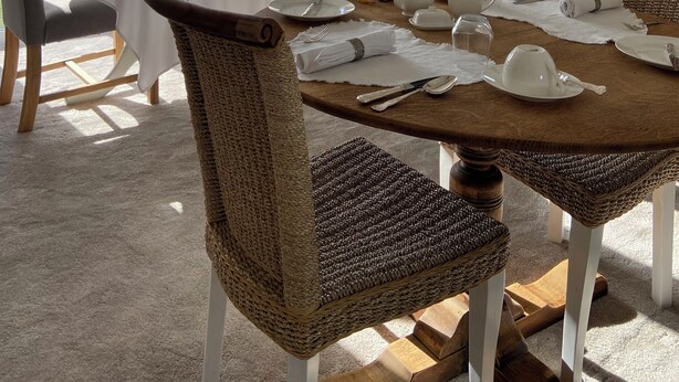 A dining area with a round table set for four, surrounded by wicker chairs. A large window offers a view of a green landscape. - Abbey Green Farm B&b, Camping & Touring Park (Whitchurch)