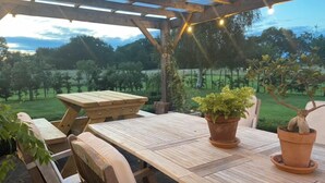 An outdoor patio with a wooden table and chairs, surrounded by potted plants and string lights. - Abbey Green Farm B&b, Camping & Touring Park (Whitchurch)