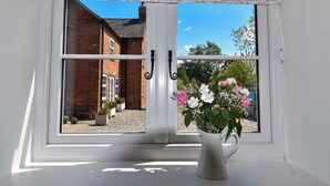 A window with a white frame and a white curtain, a vase with flowers, and a view of a brick building and a car. - Abbey Green Farm B&b, Camping & Touring Park (Whitchurch)