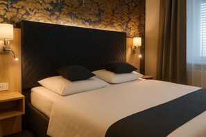 Ein ordentlich bezogenes Bett mit zwei Kissen, einem dunklen Kopfteil und zwei Wandleuchten.