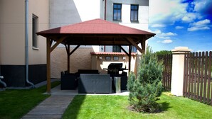 A covered patio with outdoor furniture, a barbecue grill, and a small tree. - Pension Falconi (Kolin)
