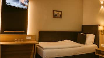 A hotel room with a bed, a bedside table with glasses, a television mounted on the wall, and a framed picture on the wall.