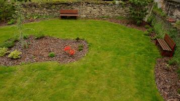 Ein gepflegter Garten mit zwei Holzbanken, einer Steinmauer und verschiedenen Sträuchern und Pflanzen.
