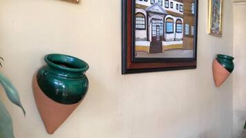 A wall with two framed paintings, a wooden shelf with green and beige ceramic pots, and a potted plant.