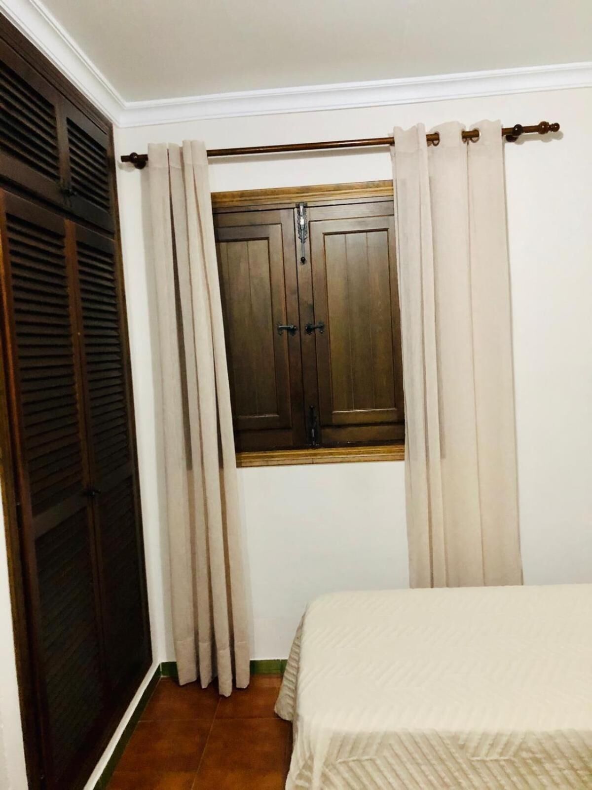 A bedroom with a window, curtains, a bed, and a wardrobe.
