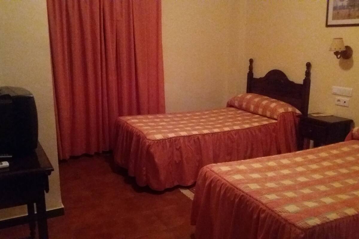 Habitación de hotel con dos camas individuales, un escritorio con televisor y una cortina roja.