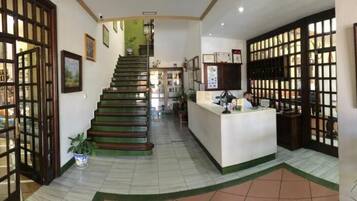 A hotel lobby with a staircase, reception desk, and decorative screens.