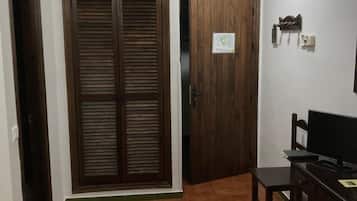 Een kamer met een houten garderobe, een bureau met stoel, een bed en een betegelde vloer.
