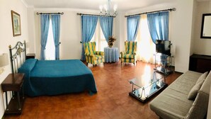 Une chambre d’hôtel avec un lit, un canapé, un téléviseur posé sur un meuble et deux fauteuils.