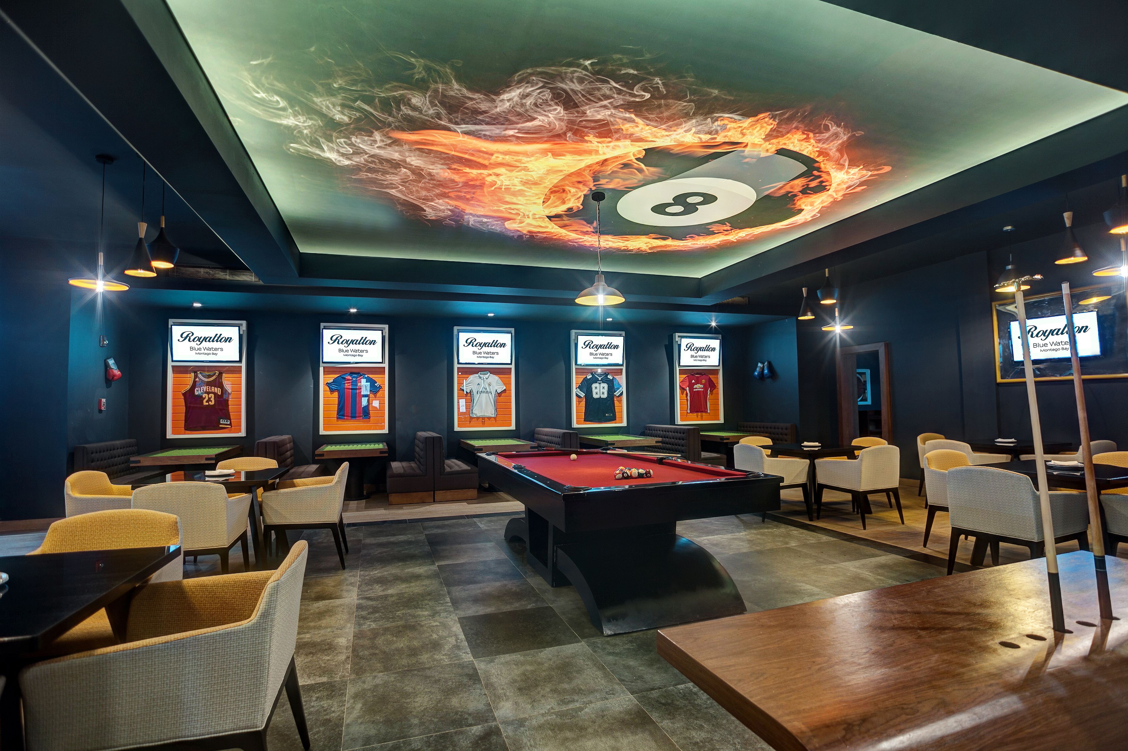 A billiards room with a pool table, chairs, and framed sports posters on the walls.
