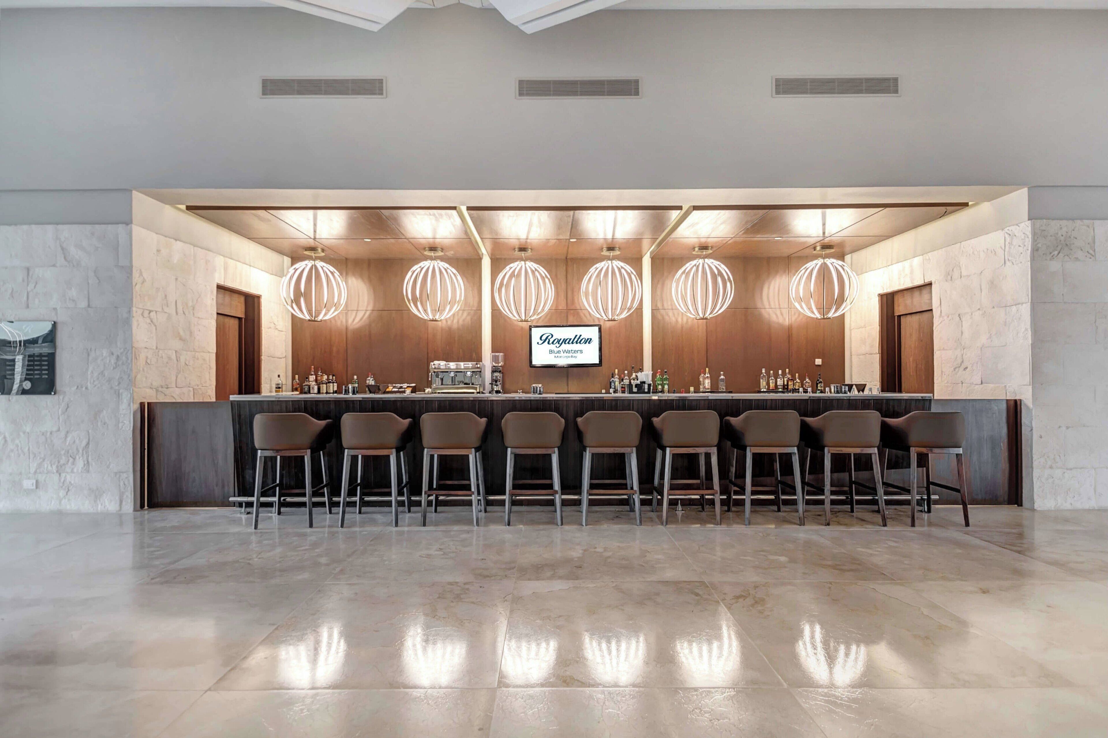 Uma área de bar com um balcão comprido, vários bancos e iluminação pendente.