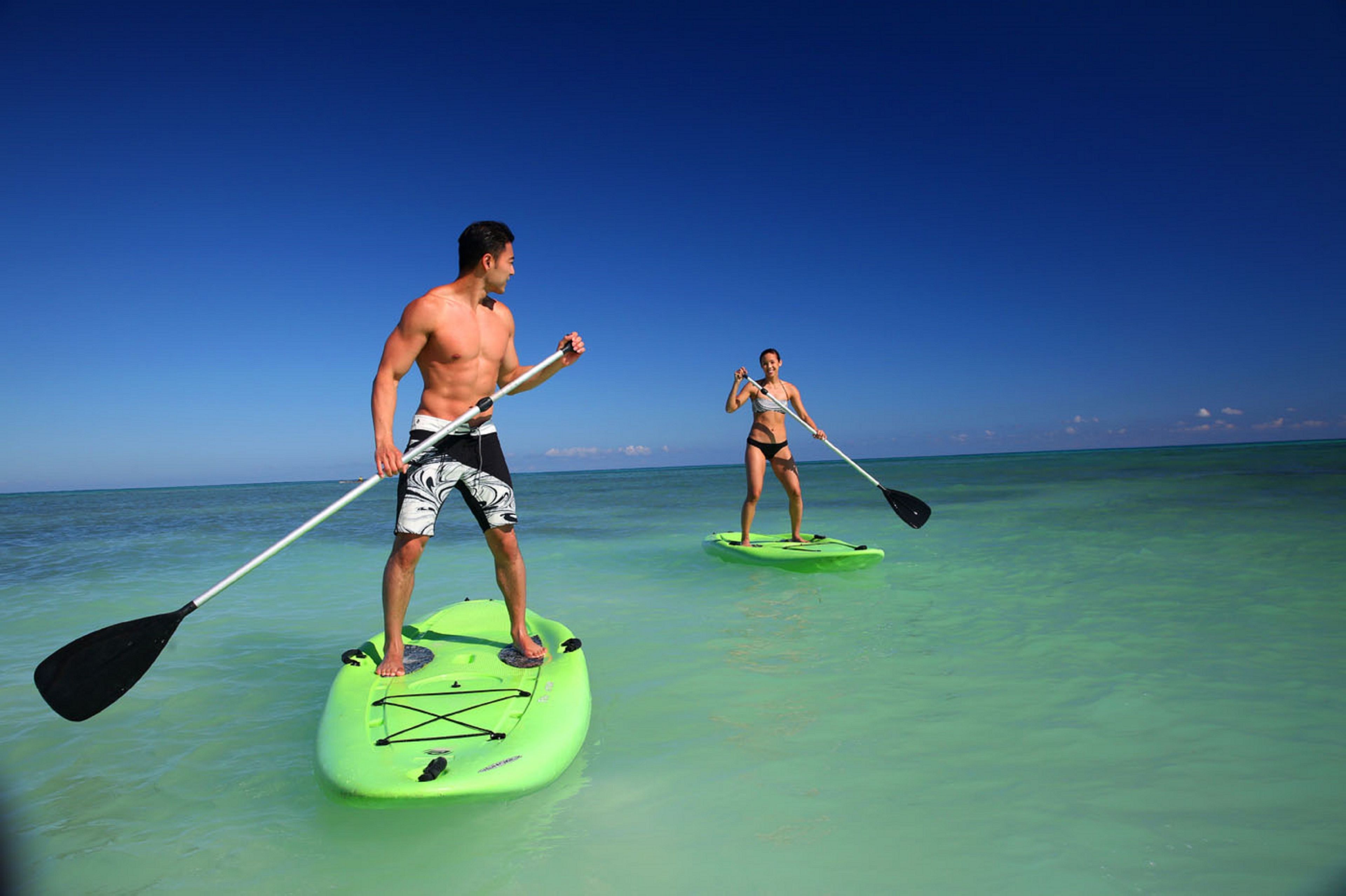 Two people paddleboarding on a clear turquoise sea with a clear sky.