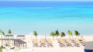 Une plage avec des chaises longues et des parasols, une piscine et une vue sur l’océan.