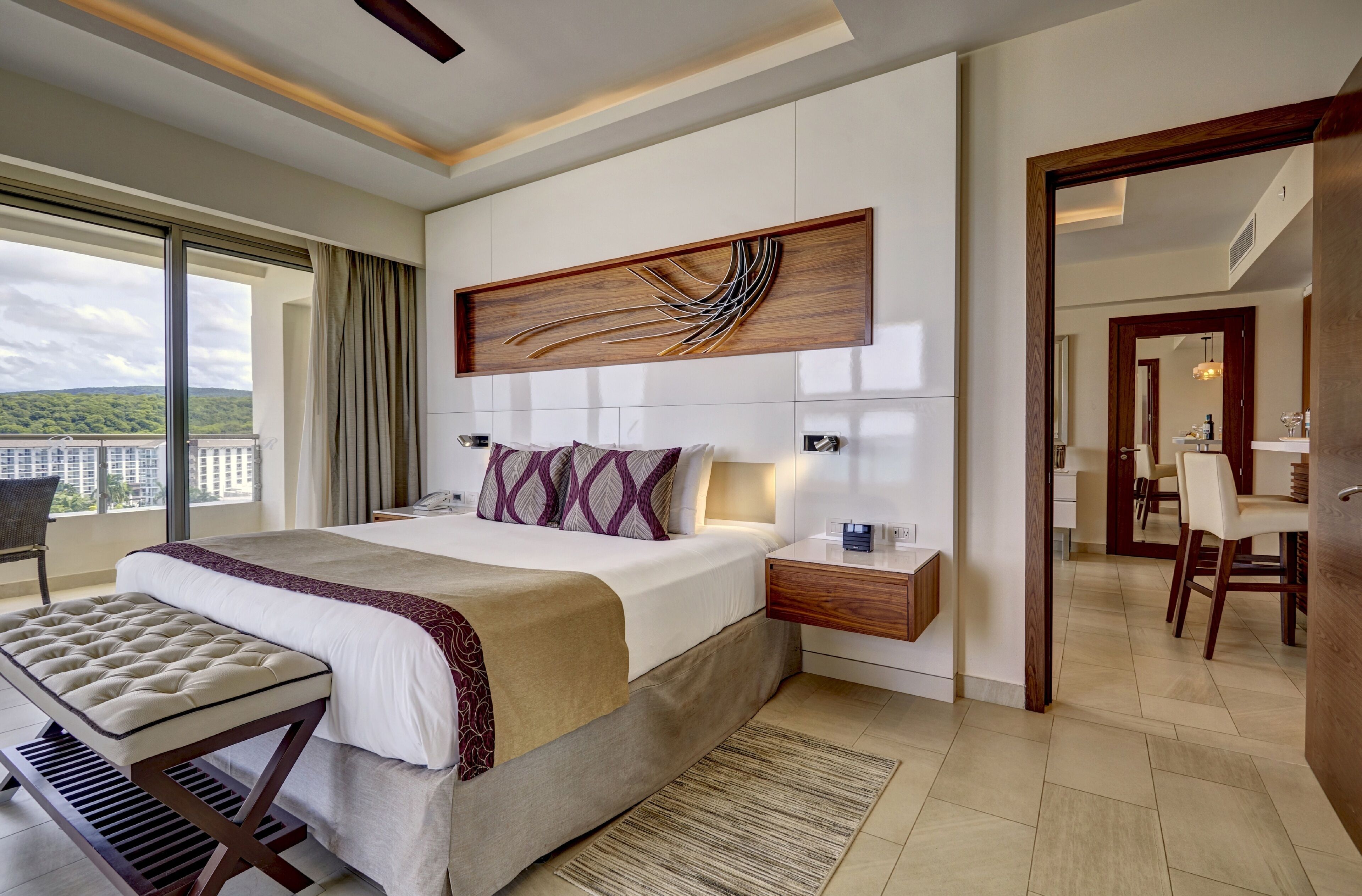 A modern hotel room with a large bed, a desk, and a view of the city.