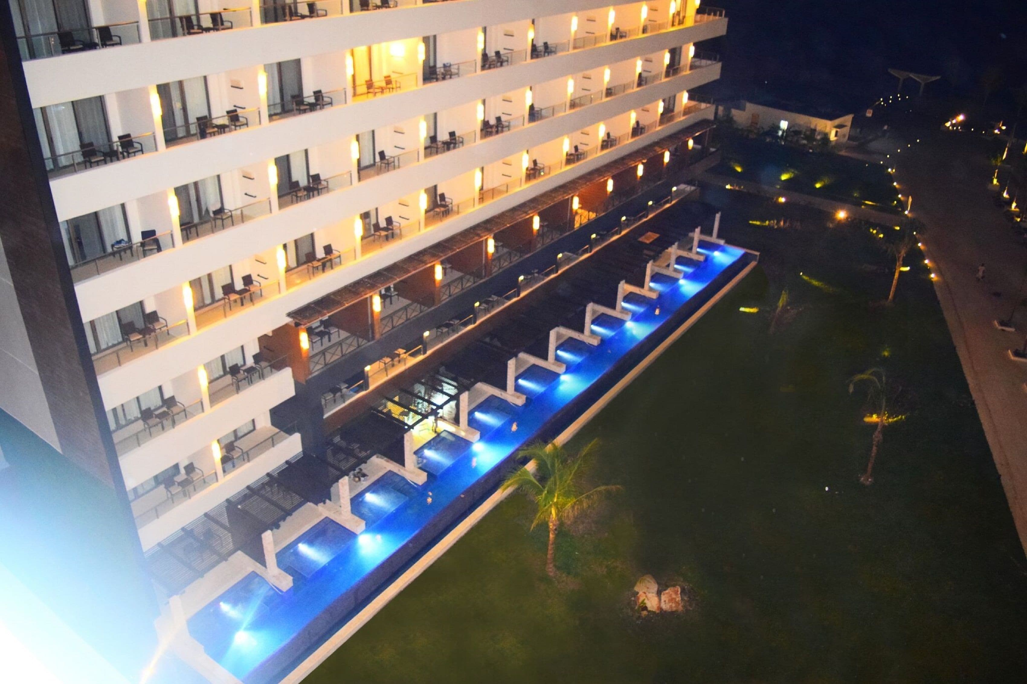A multi-story hotel with balconies, a swimming pool, and a well-lit outdoor area.