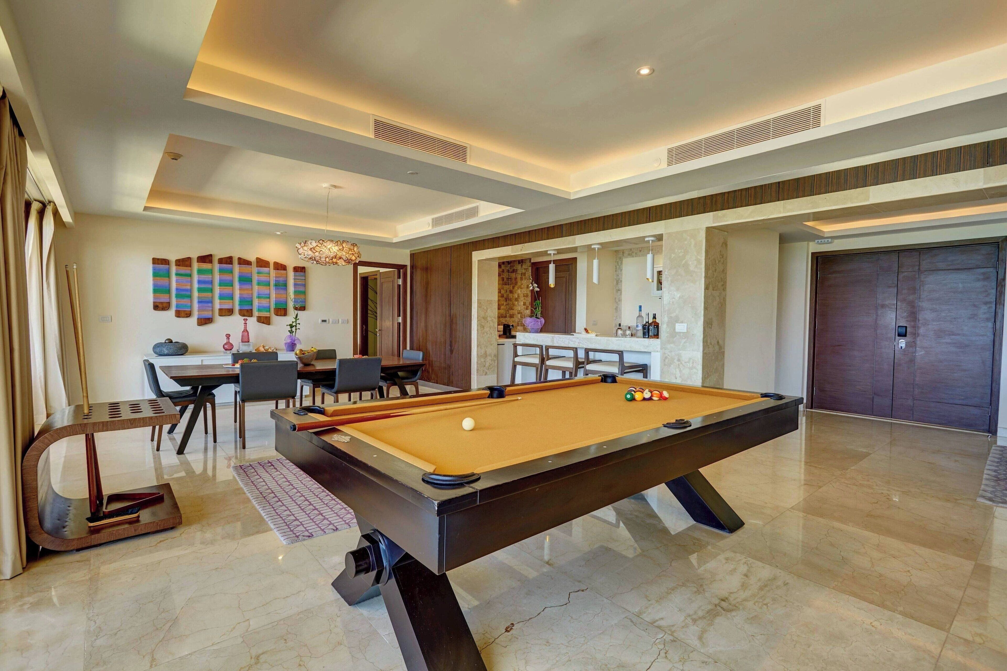 Un espace piscine intérieur moderne, comprenant une table de billard, des sièges et un bar.