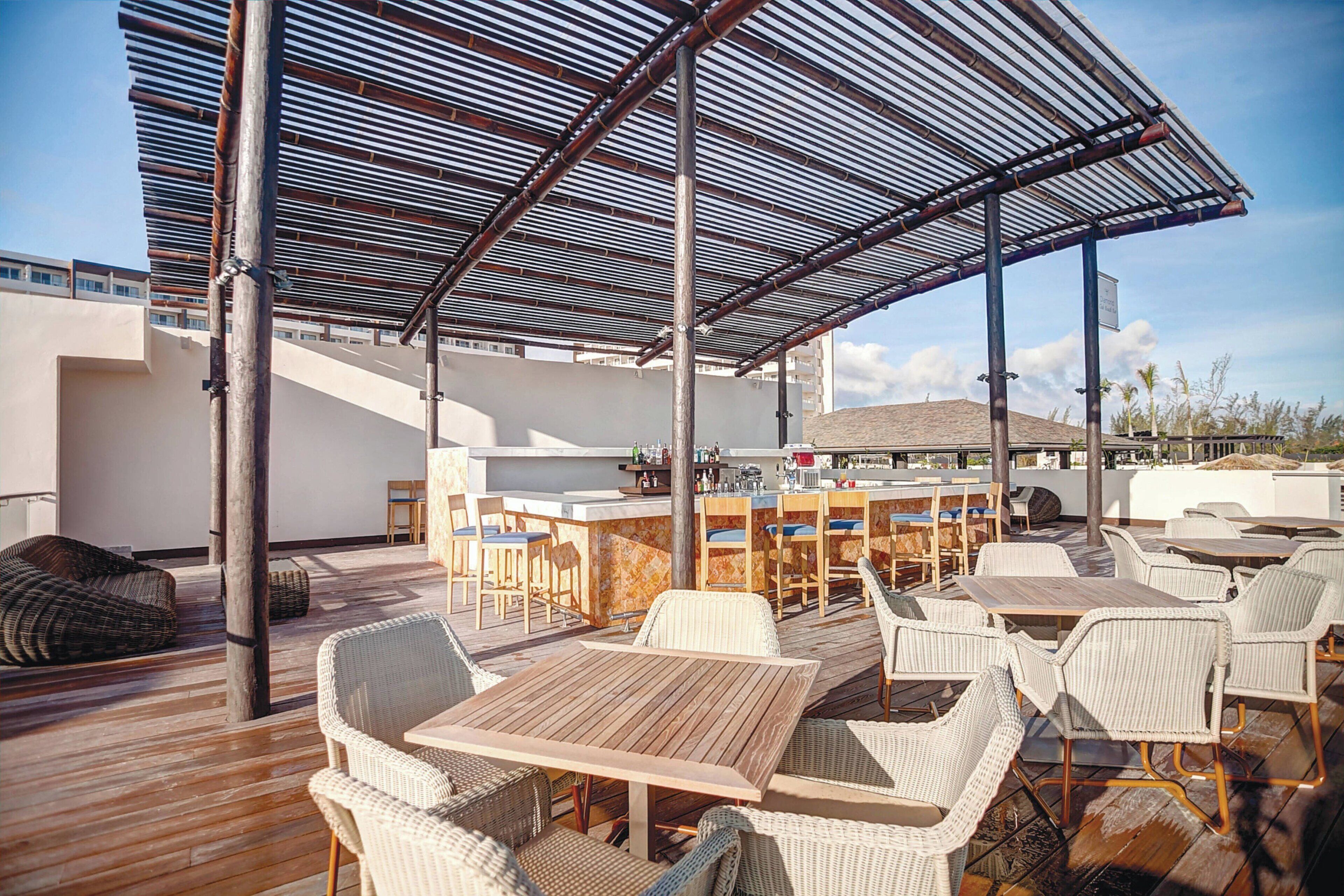 An outdoor patio with wooden tables and wicker chairs, a bar area, and a covered seating area with a metal roof.