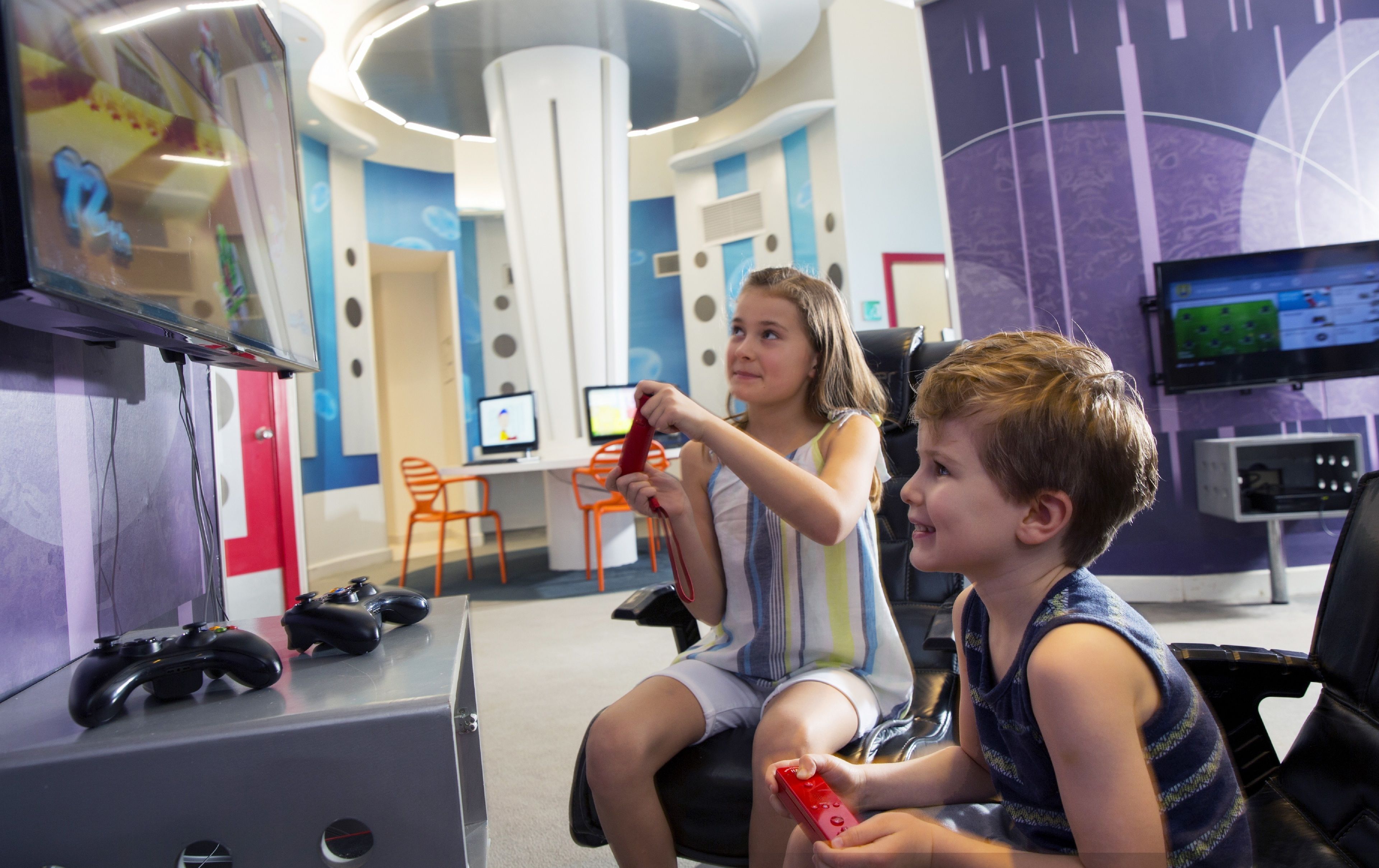 A gaming area with two children playing video games, a TV screen, and gaming consoles.