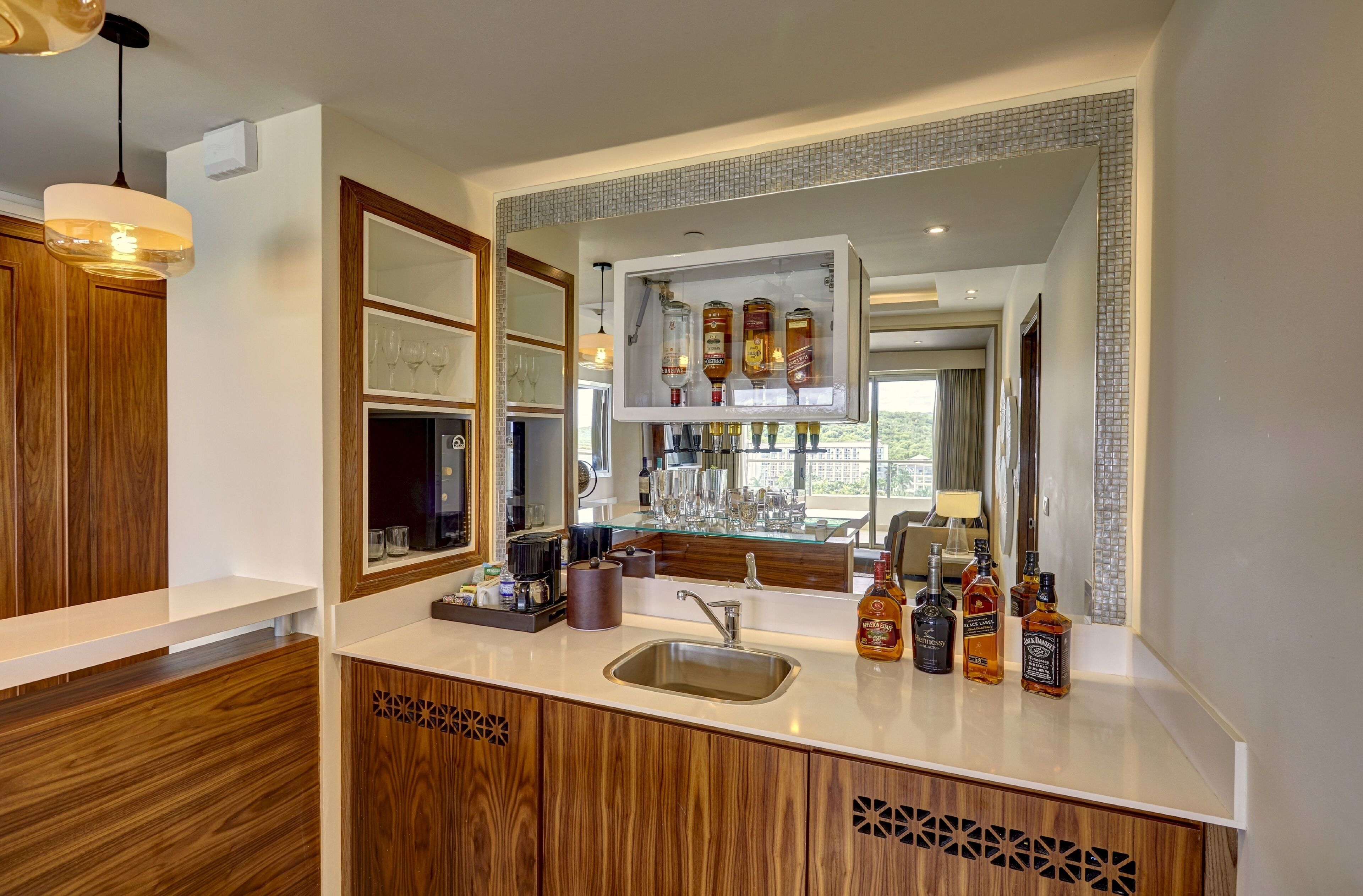 A modern kitchen with wooden cabinetry, a built-in bar area with a large mirror, and a variety of glassware and bottles.