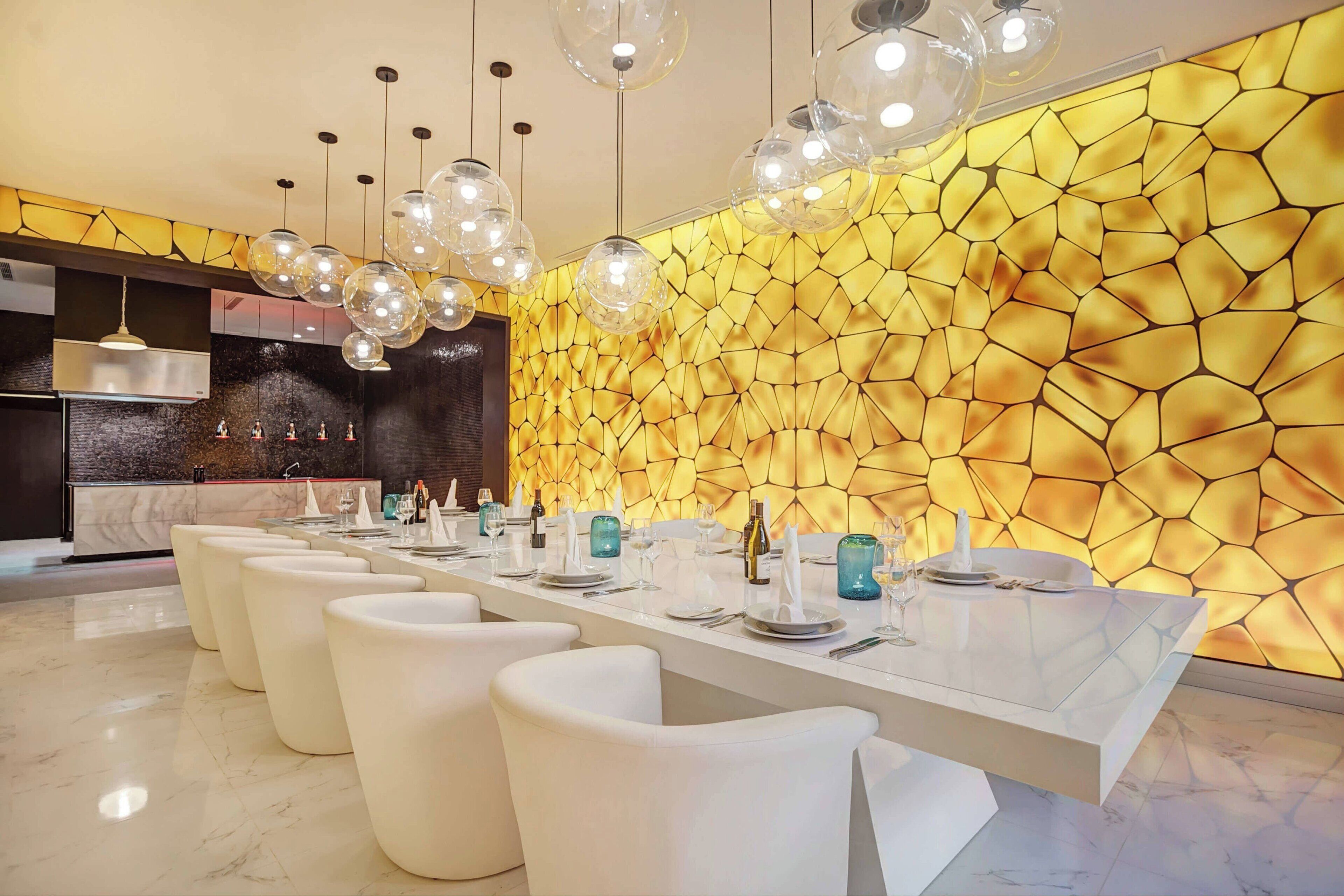 A modern dining area with a long table, white chairs, and a unique geometric wall design.