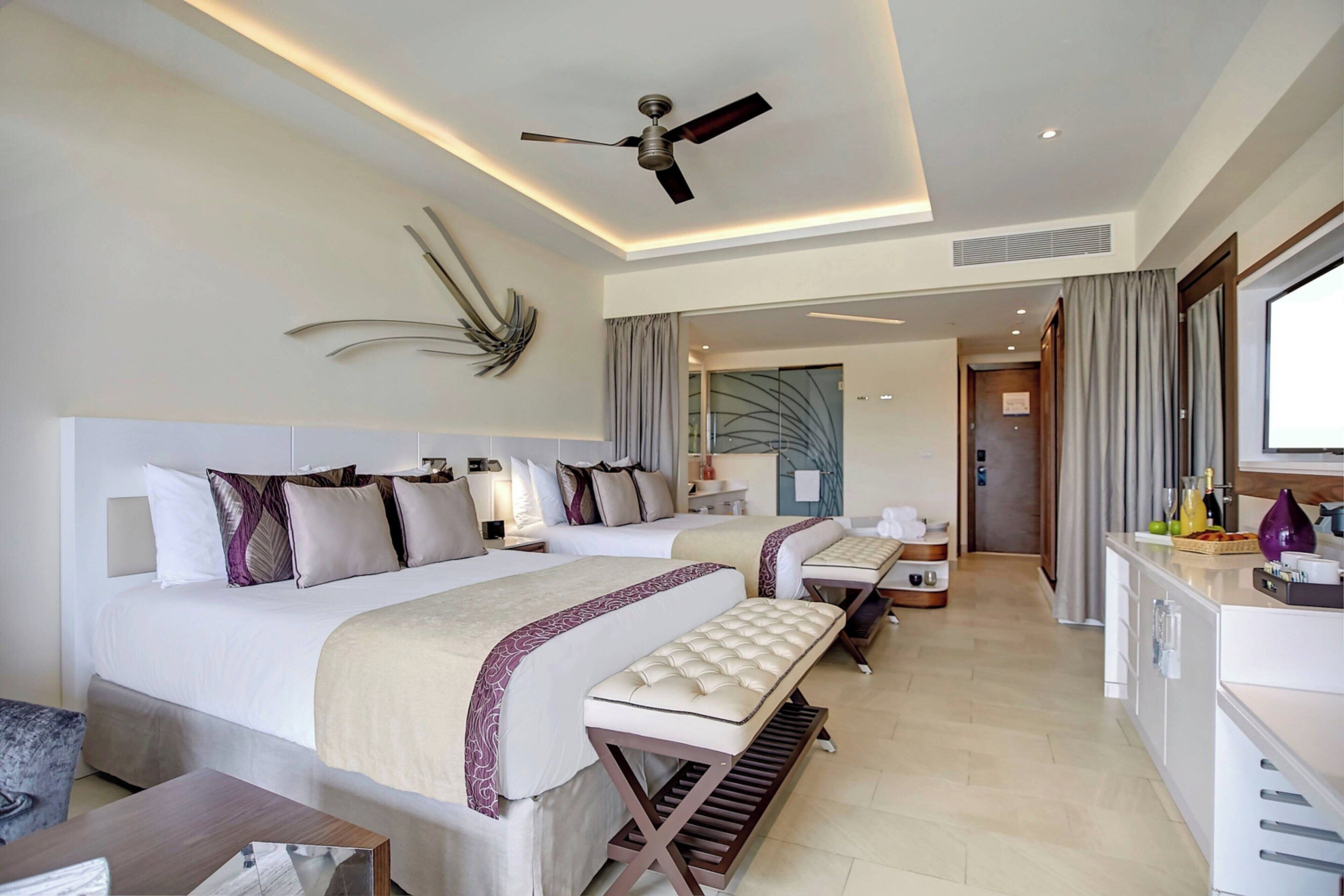 Een moderne hotelkamer met twee bedden, een zithoek, een kitchenette en een plafondventilator.