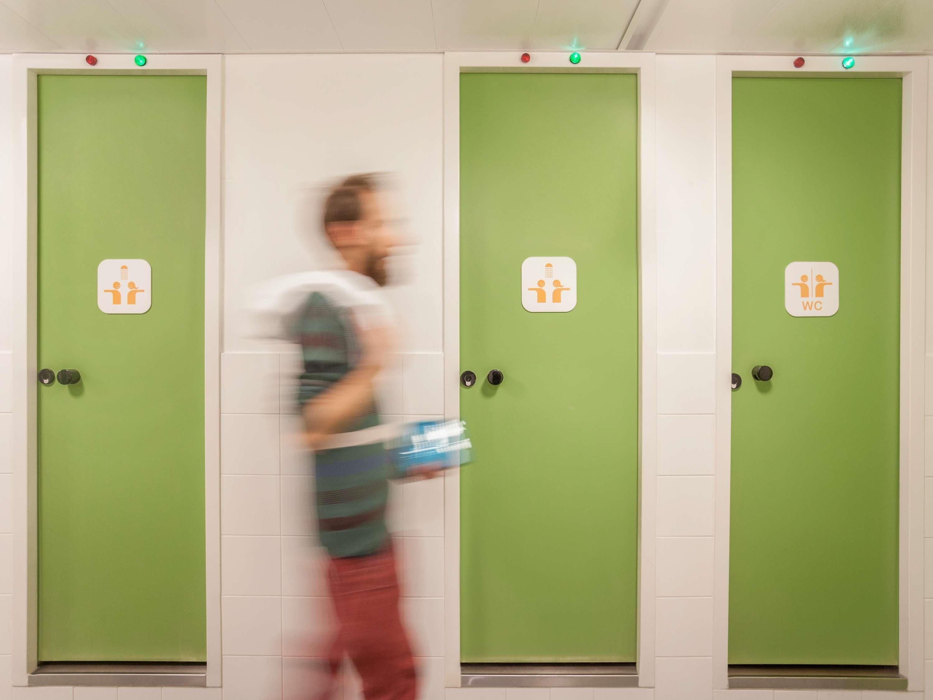 Una hilera de puertas verdes con símbolos de baño, indicando baños públicos.