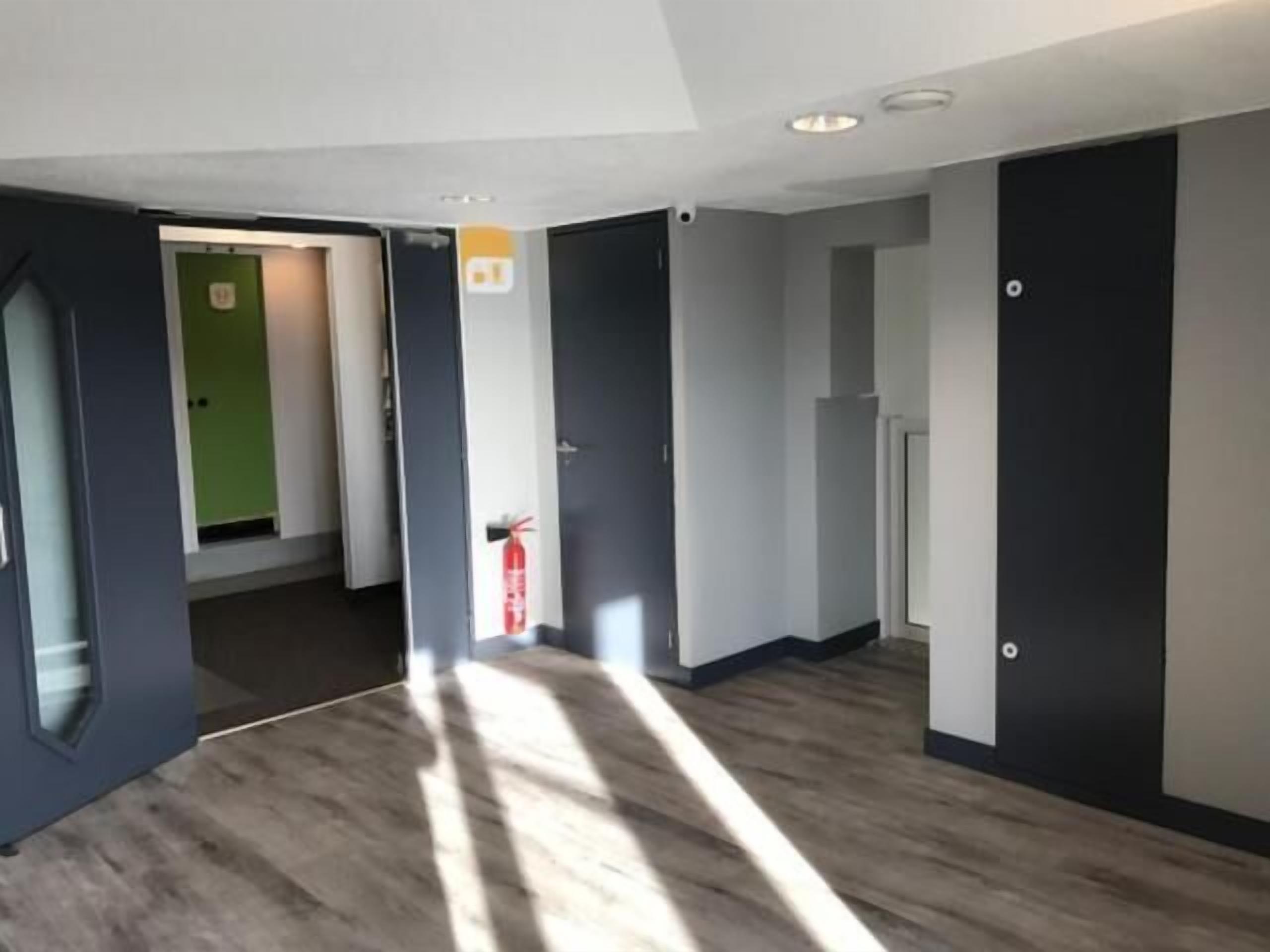 A hallway with a wooden floor, grey walls, and a green door at the end.