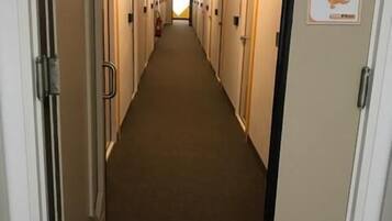 Un corridoio d'albergo con porte su entrambi i lati, pavimento rivestito di tappeto e una insegna sulla porta destra.