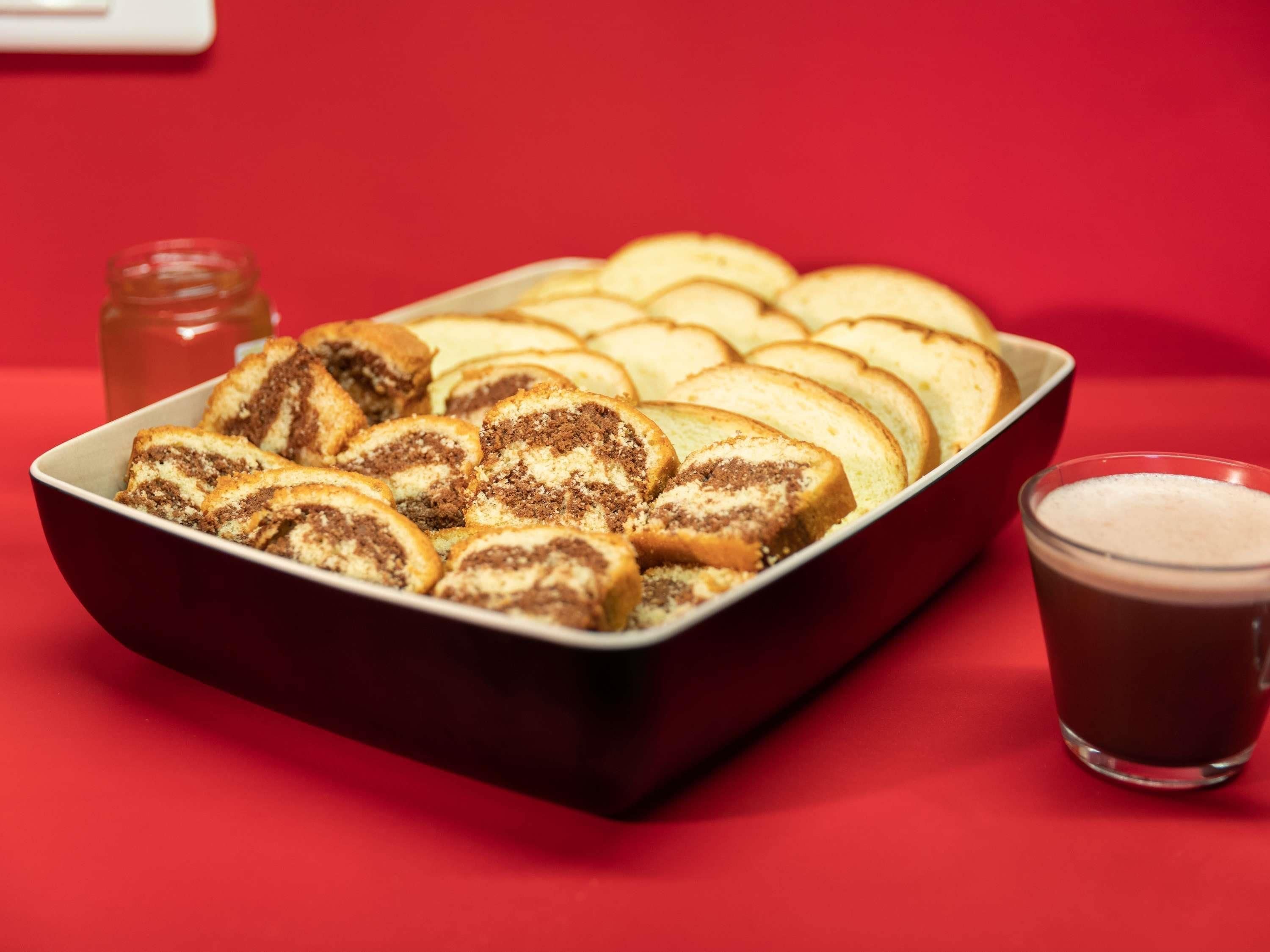 A tray of sliced pastries and a glass of dark beverage on a red surface.