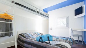 Quarto com uma cama de solteiro, uma escrivaninha com cadeira e uma televisão na parede.