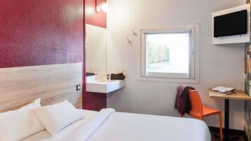 Habitación de hotel con cama, lavamanos, silla, escritorio y televisor montado en la pared.