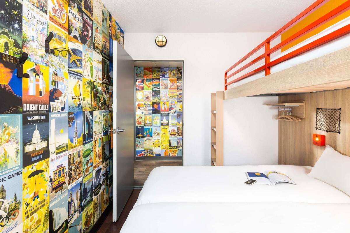 A bedroom with a bunk bed, a wall of travel posters, a door, and a small window.