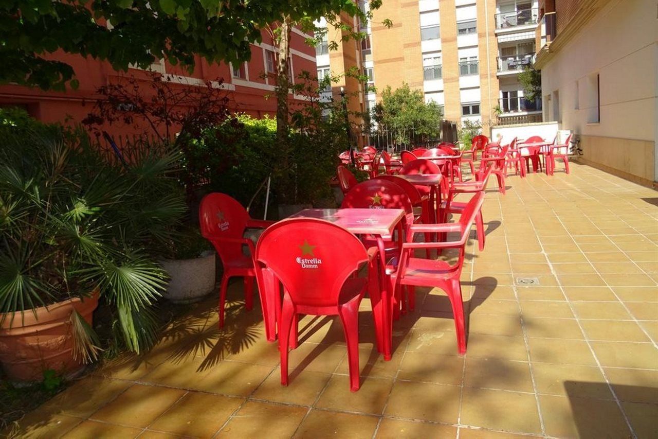 Un'area patio esterna con sedie e tavoli di plastica rossa, circondata da piante in vaso e un edificio sullo sfondo.