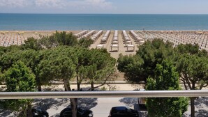 A beach with rows of umbrellas and sun loungers, a parking area with cars, and a view of the sea. - Hotel Ambra (Lignano Sabbiadoro)