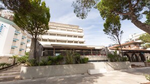 A multi-story hotel with a modern architectural design, featuring a prominent entrance and a landscaped area with trees and plants. - Hotel Ambra (Lignano Sabbiadoro)