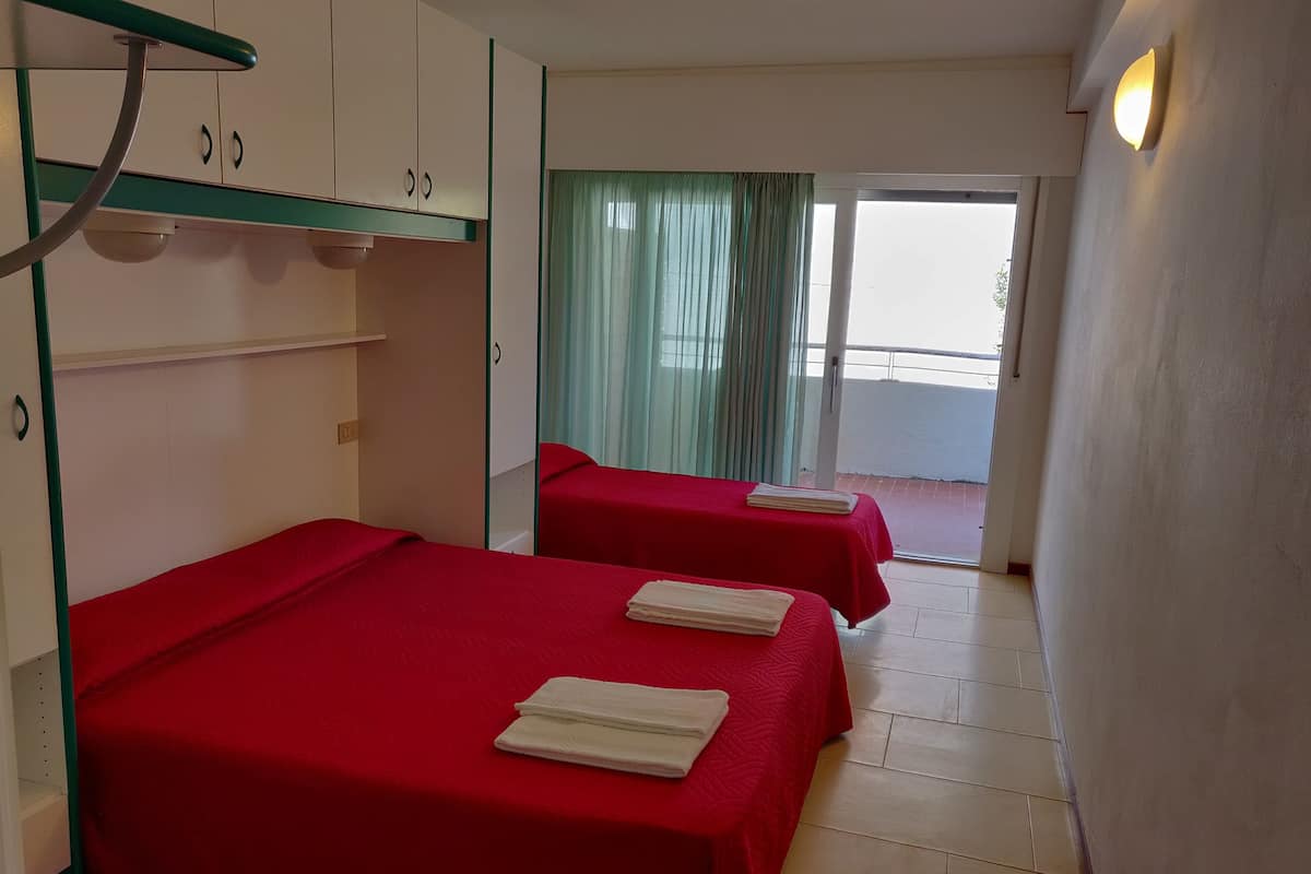 Quarto de hotel com duas camas, varanda e vista para o exterior.