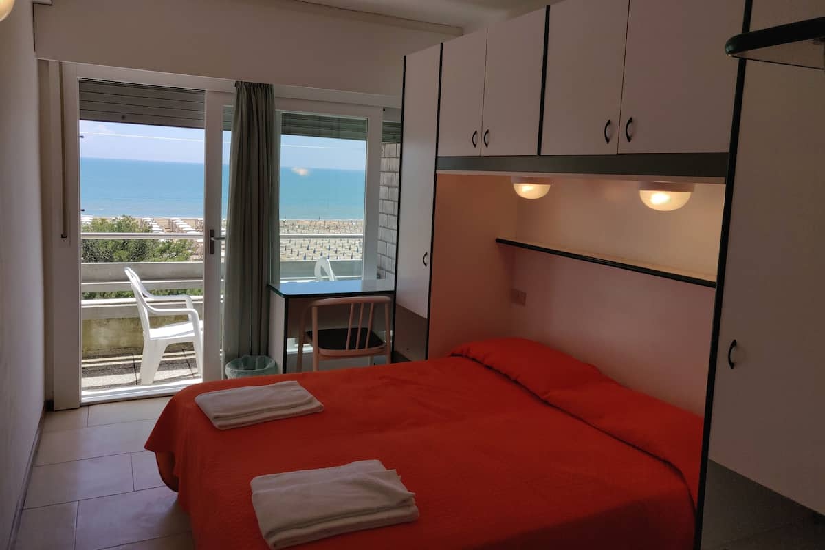 Quarto com cama, escrivaninha e vista para a praia.